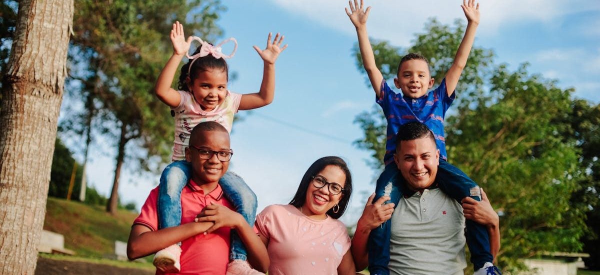 A joyful family spending quality time outdoors with kids on parents' shoulders.