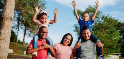 A joyful family spending quality time outdoors with kids on parents' shoulders.