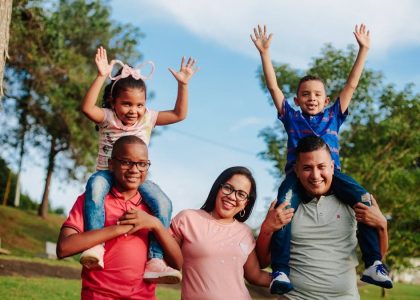 A joyful family spending quality time outdoors with kids on parents' shoulders.